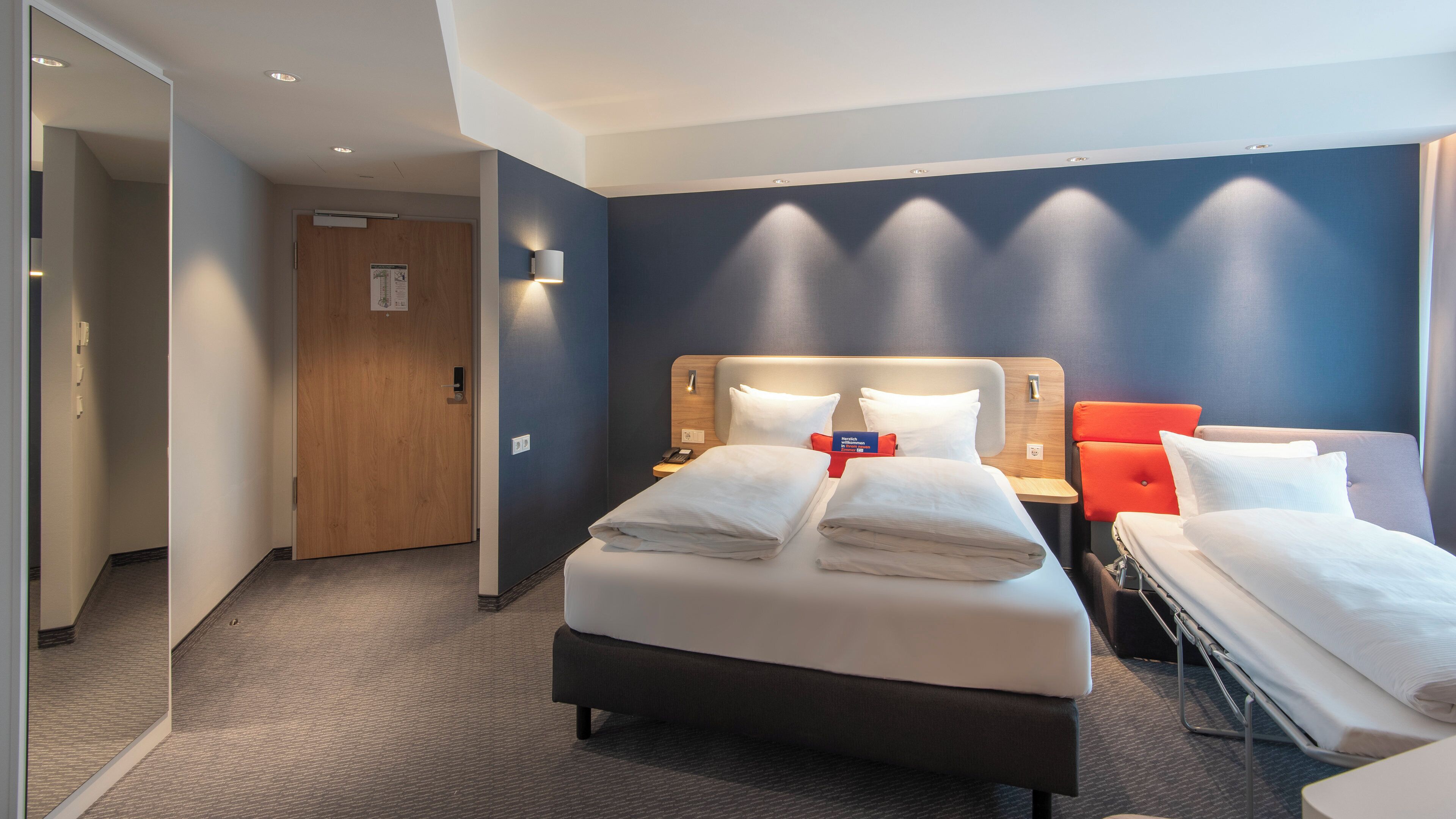 A hotel room with a large bed, bedside tables, a nightstand, and a mirror.