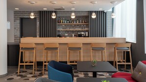 Een moderne bar met een lange toonbank, verschillende barkrukken en een divers aanbod aan flessen op de planken.