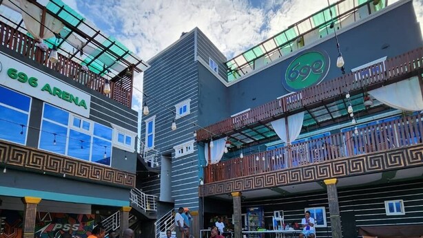 A courtyard with a mosaic floor, a bar area, and a building with a sign reading "696 ARENA". - 696 Arena Aflao (Aflao)