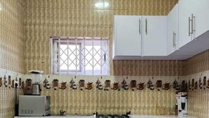 A compact kitchen with patterned wallpaper, a gas stove, white cabinets, and a small window. - 696 Arena Aflao (Aflao)