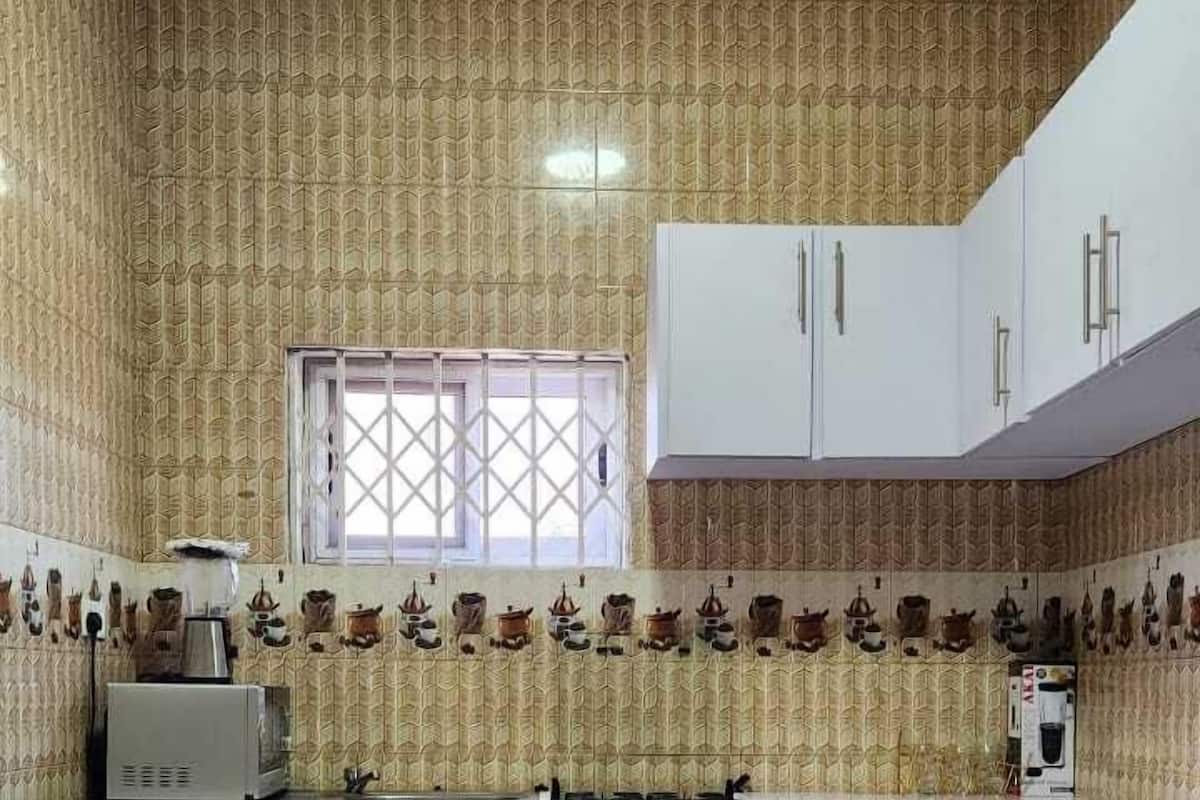 Una cuina petita amb paper tapet i un forn de gas, armaris blancs i una finestra.