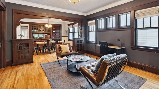 A spacious living room with a wooden floor, leather chairs, a coffee table, and a dining area with a wooden table and chairs. - Just A Short Stroll to Lake Harriet & Restaurants! (Minneapolis)