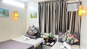 A hotel room with two beds, each with a pillow and a neatly folded towel. There is a small table with a plant and a cup, and a wall-mounted air conditioner. - International Inn (Kowloon)