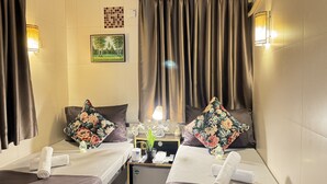 A hotel room with two beds, each with a floral pillow, a small table with a lamp, and a picture on the wall. - International Inn (Kowloon)