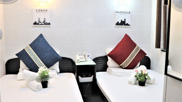 A hotel room with two beds, each with a pillow, a small table with a phone and a plant, and a wall with cityscape posters. - International Inn (Kowloon)