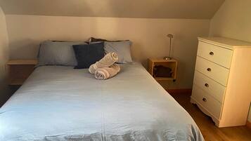 Une chambre à coucher avec un lit, des oreillers, une table de chevet en bois, une lampe et une commode.