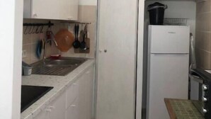 Eine kleine Küche mit weißen Schränken, einem Spülbecken, einem Herd und einem Kühlschrank.
