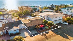 An aerial view of a residential area with houses, a parking lot, and a view of the ocean.