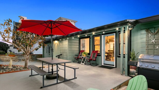 An outdoor patio area with a table and chairs, a red umbrella, and a barbecue grill.