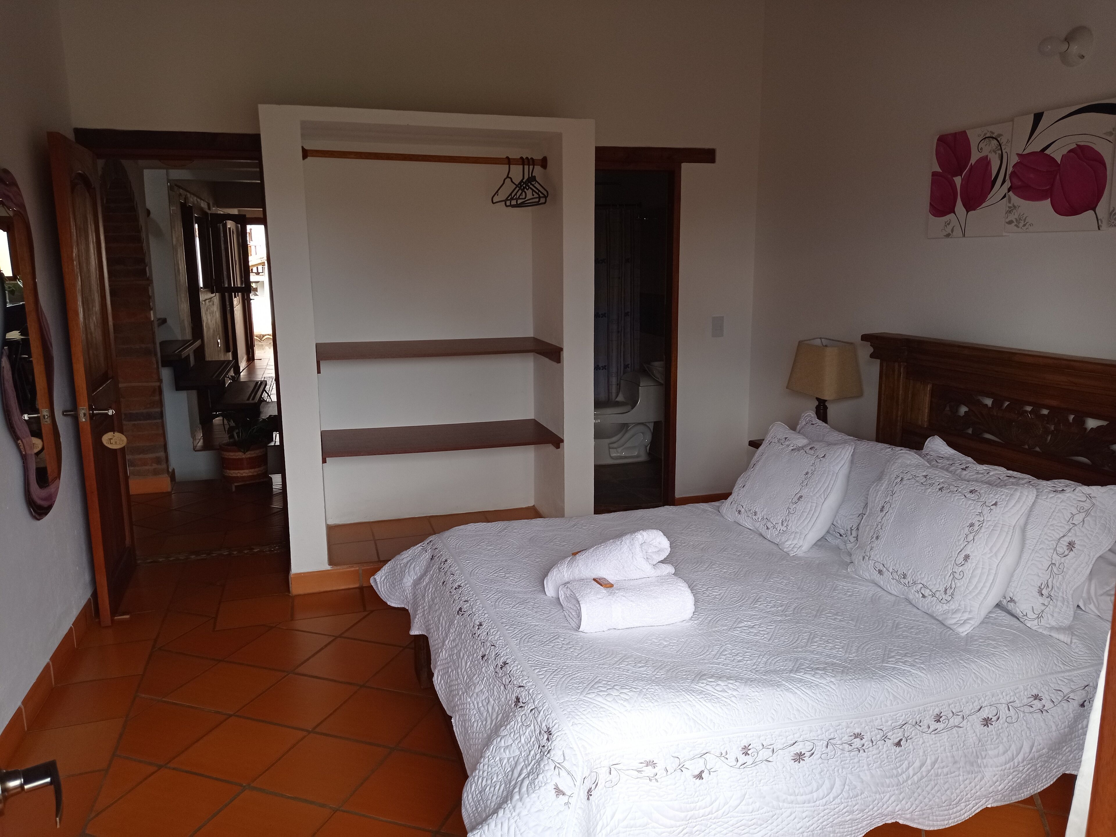 Un dormitorio con una cama, cabecera de madera, mesita de noche, lámpara y un cuadro en la pared.