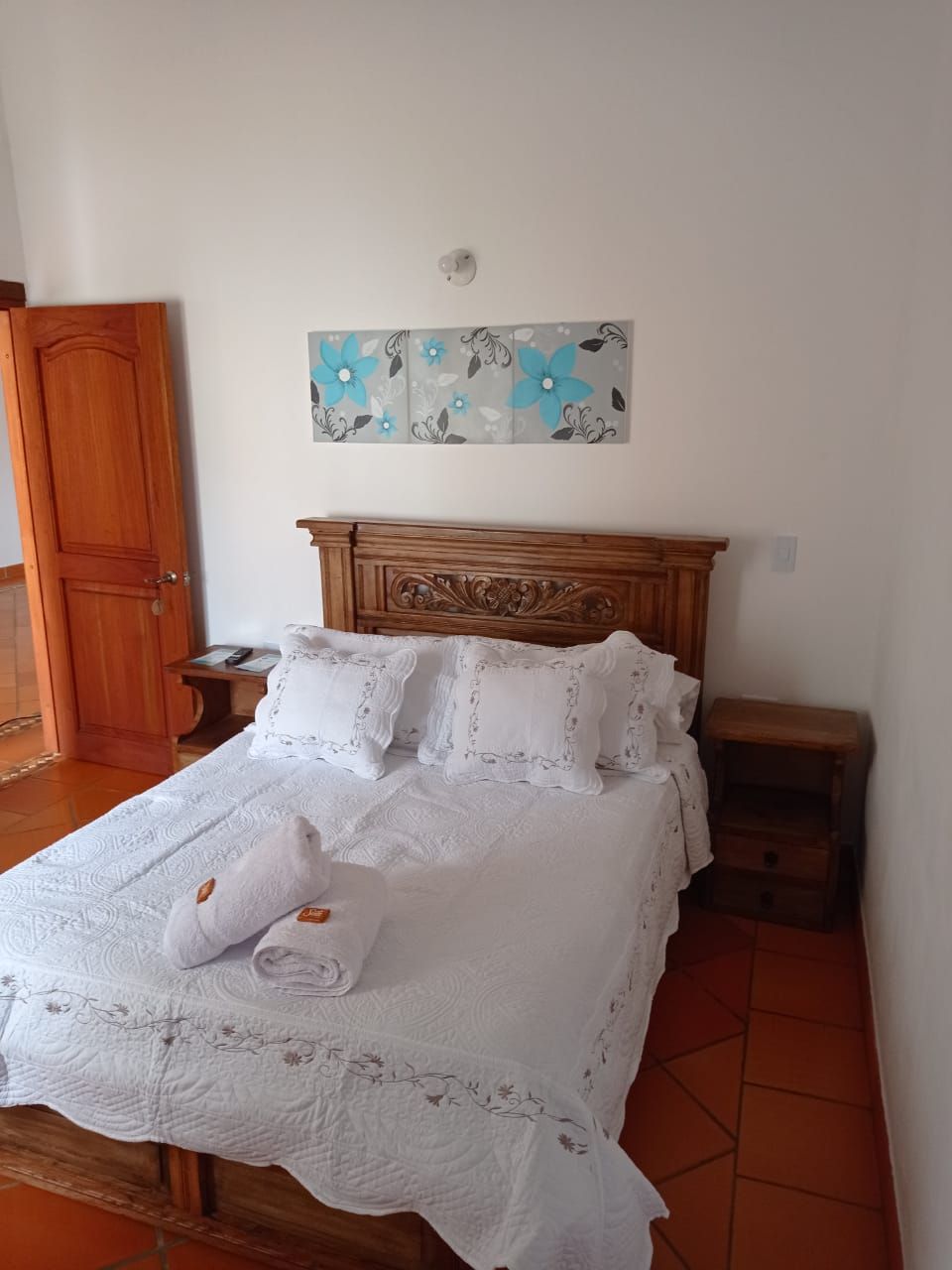 Ein Schlafzimmer mit einem hölzernen Bett, weißen Leinentüchern, einer Wanddekoration, einem Nachttisch aus Holz und einer Holztür.