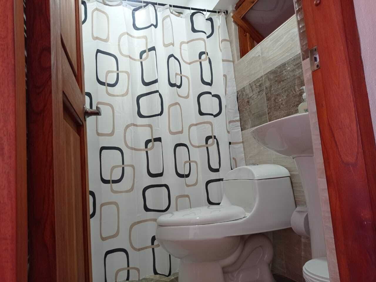 Ett badrum med en toalett, en duschdraperi med ett geometriskt mönster och en kaklad vägg.