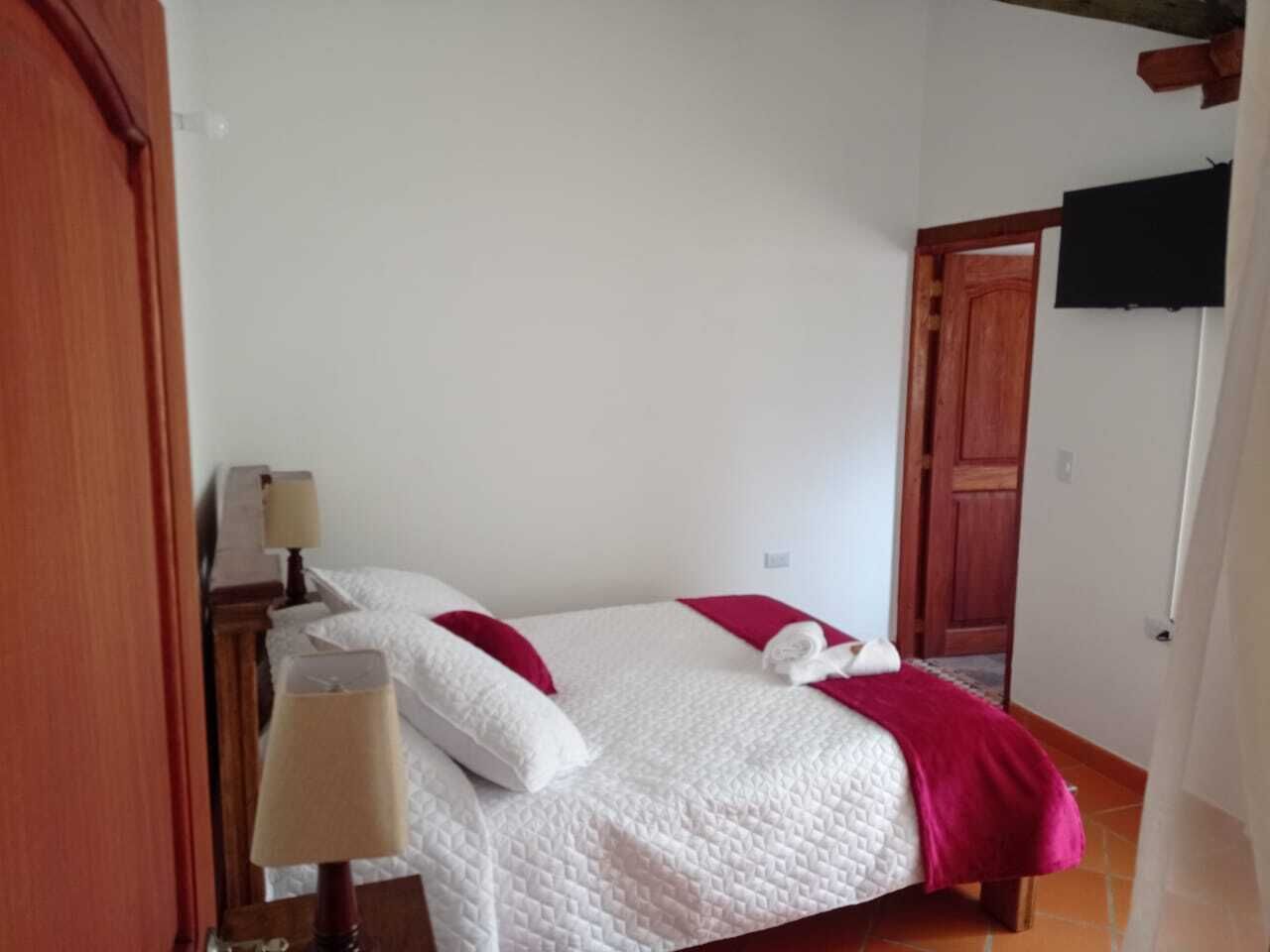 Un dormitorio con una cama, una mesita de noche, una lámpara y un televisor en la pared.