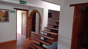 A staircase with wooden steps leading to a landing, a door with a brick archway, and a green sign indicating an emergency exit. - CASA HOTEL LA VILLA DEL ROSARIO (Villa de Leyva)