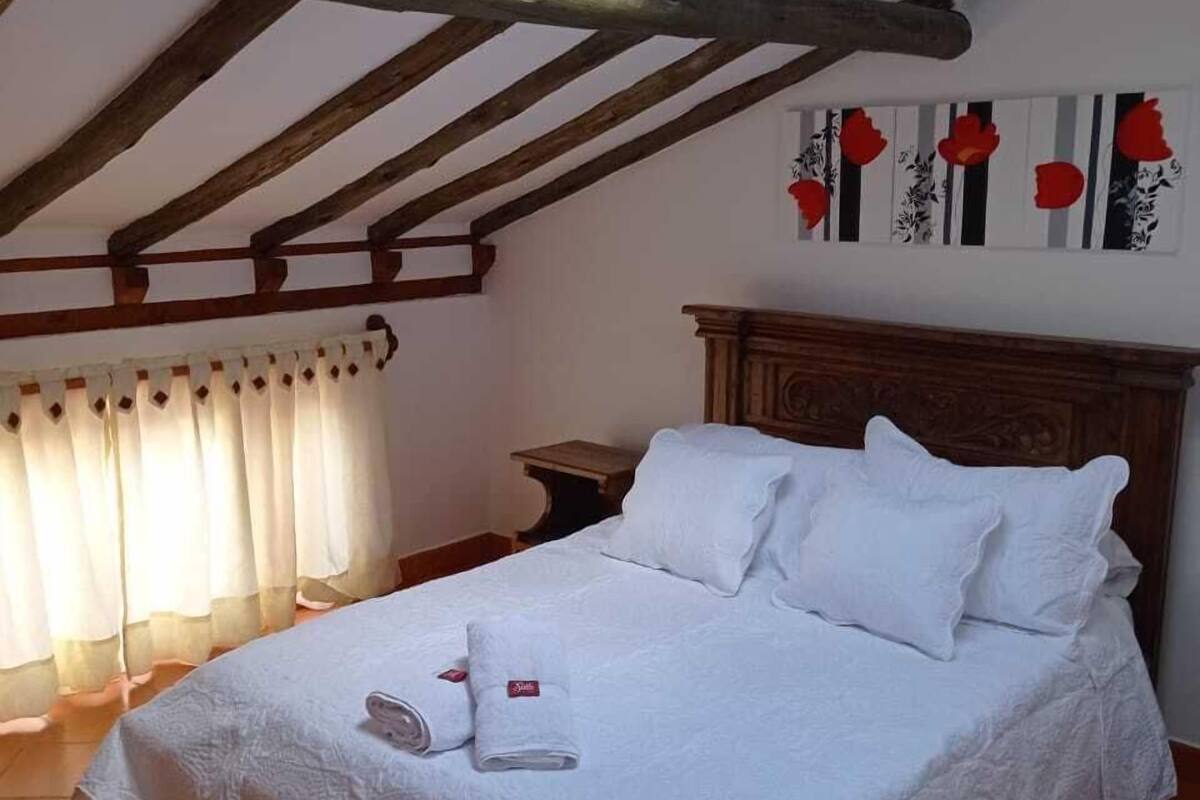 Une chambre à coucher avec un plafond en bois, un lit recouvert de draps blancs, une table de chevet et une fenêtre avec des rideaux.