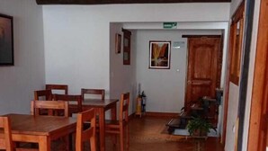 A dining area with wooden tables and chairs, a tiled floor, and a hallway leading to a door. - CASA HOTEL LA VILLA DEL ROSARIO (Villa de Leyva)
