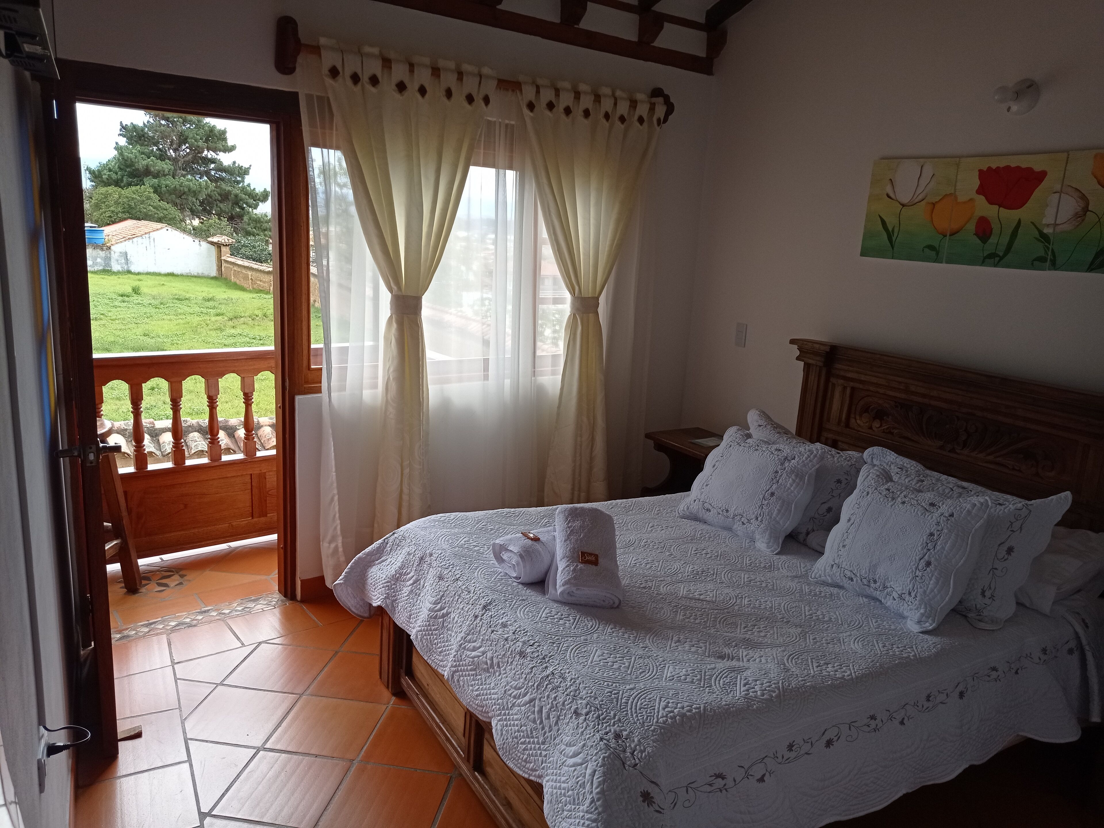 Une chambre à coucher avec un lit, des rideaux, un tableau et une vue sur un jardin.