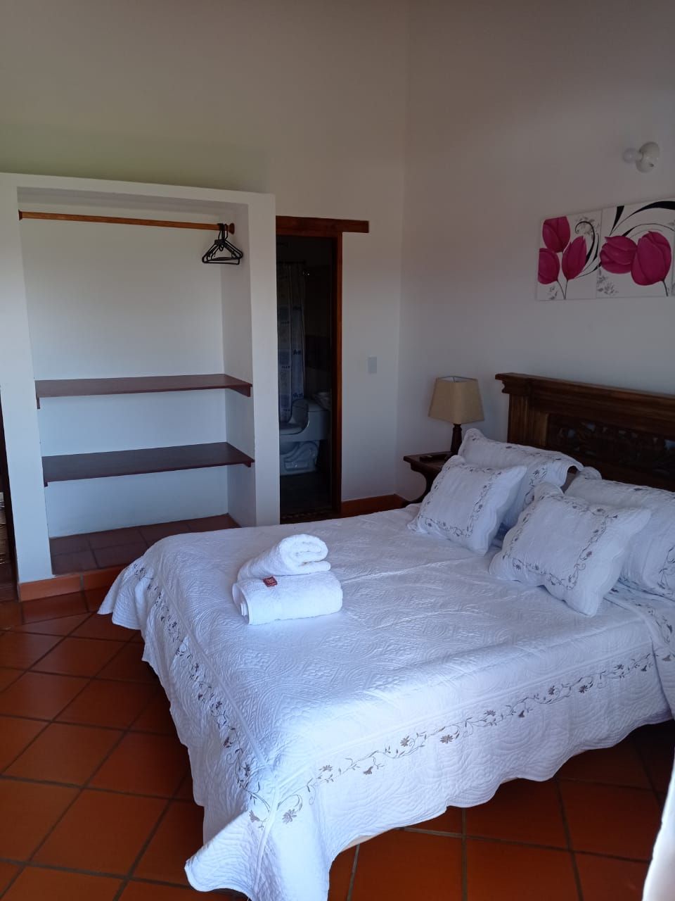 Een slaapkamer met een bed, nachtkastje, lamp, kledingkast en een deur naar een badkamer.