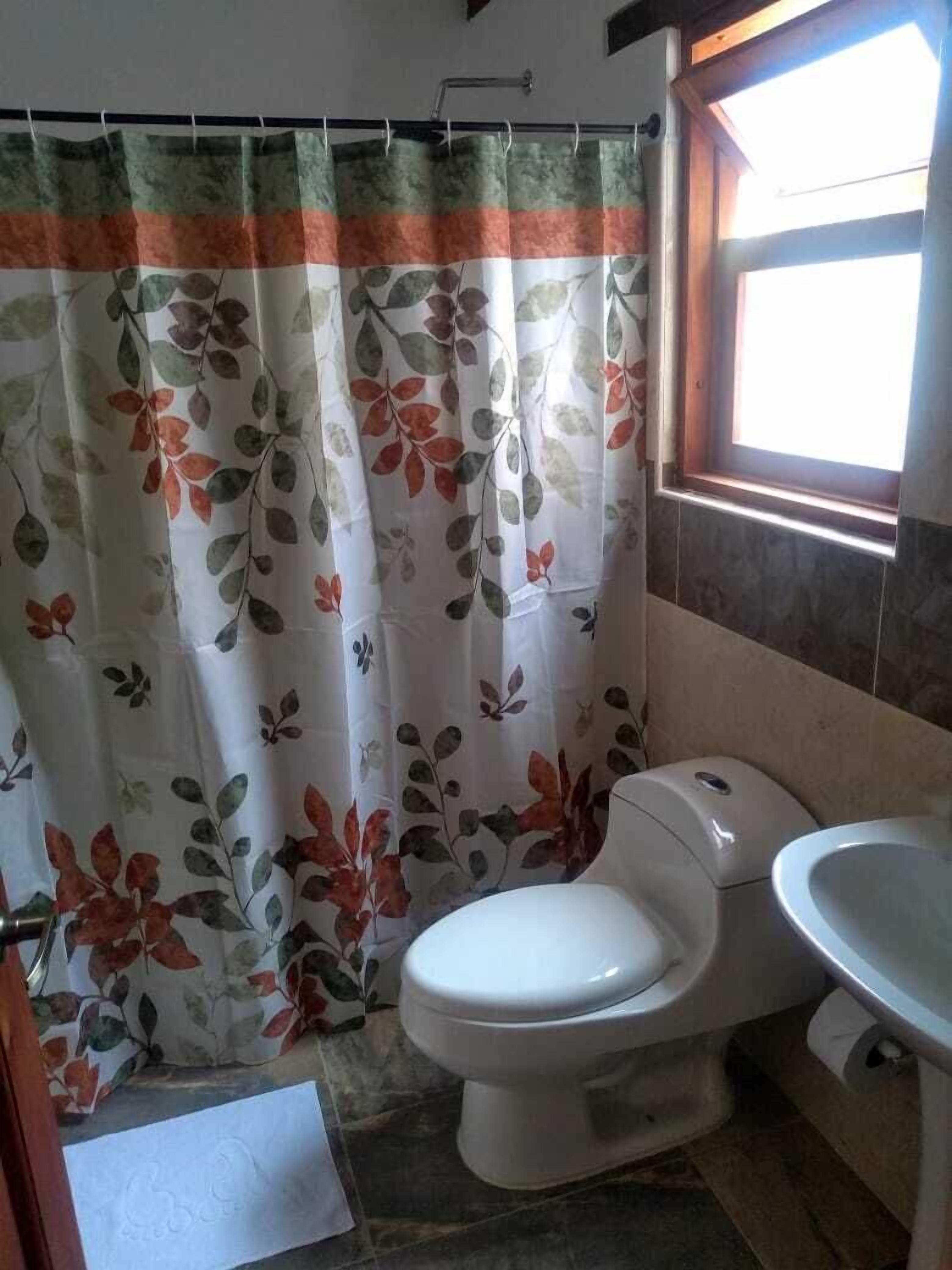Et badeværelse med bruseforhæng med bladmotiv, toilet og håndvask.