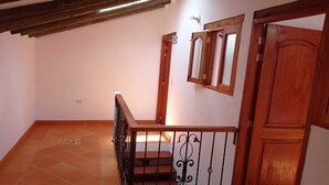 A staircase with a wooden handrail and black balusters, leading to a landing with a wooden door and a mirror. - CASA HOTEL LA VILLA DEL ROSARIO (Villa de Leyva)