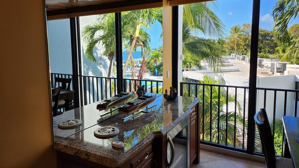 Una cocina con un amplio ventanal que da a una zona de piscina, con techo de madera y encimera de mármol.