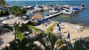 Un puerto deportivo con barcos amarrados, una zona de playa con sillas de descanso y sombrillas, y una vista despejada del agua.