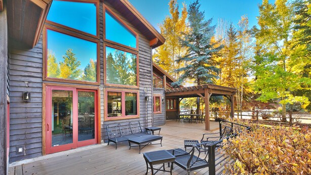 Terraza de madera con mobiliario exterior y ventanas amplias que dan a un bosque.