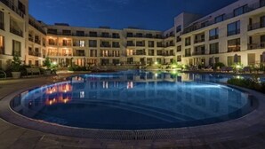 Pátio de hotel com piscina, várias varandas e edifícios bem iluminados.