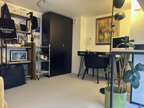 Een kamer met een bureau, stoel, boekenplanken met diverse spullen, een zwarte kast en een schilderij aan de muur.