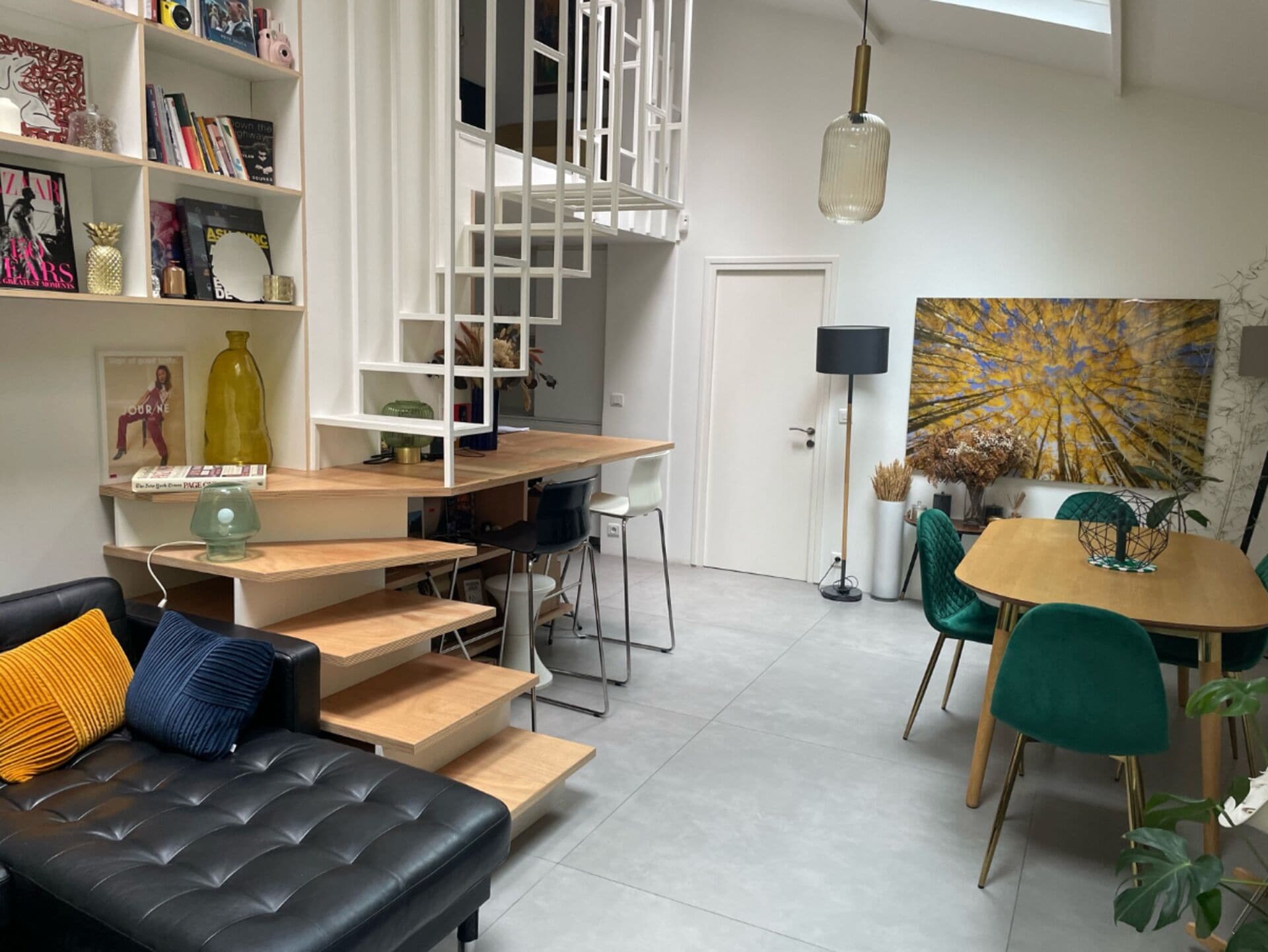 Ein modernes Wohnzimmer mit einer schwarzen Ledersofa, einem Holzesstisch mit Stühlen, einer Treppe und einem Bücherregal.