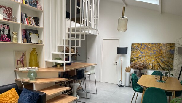 Ein modernes Wohnzimmer mit einer schwarzen Ledersofa, einem Holzesstisch mit Stühlen, einer Treppe und einem Bücherregal.