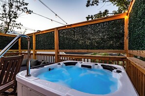 A hot tub on a wooden deck with a wooden railing and a view of a hedge.