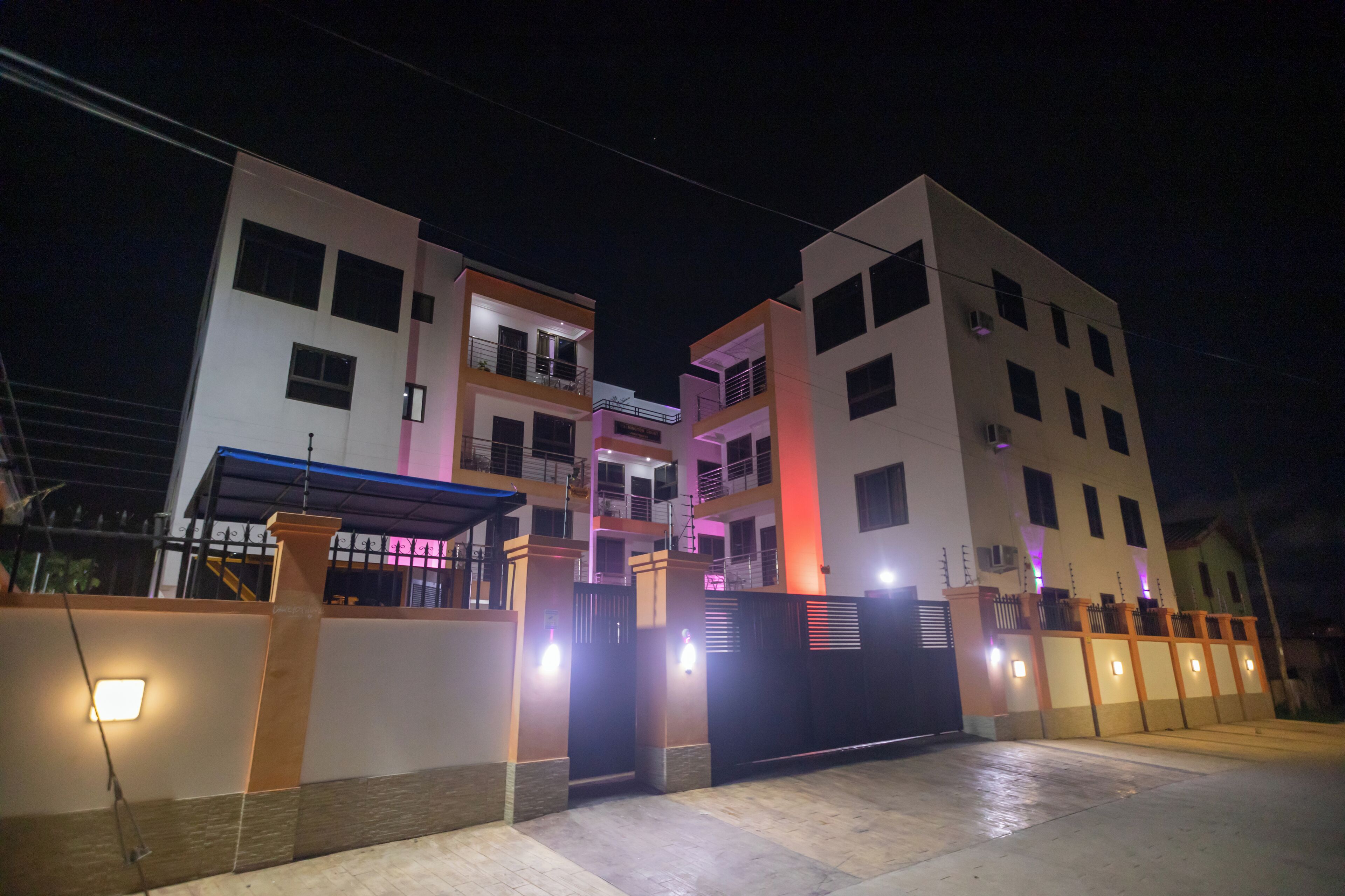 A multi-story residential building with a gated entrance, illuminated by exterior lights.