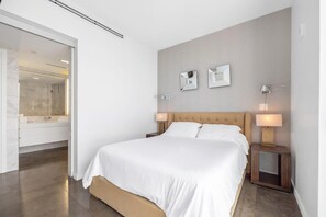 A modern bedroom with a large bed, bedside lamps, and a bathroom visible through an open door.