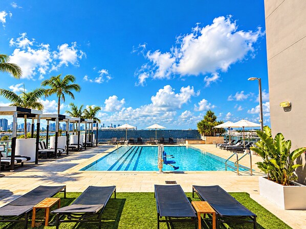 A pool area with lounge chairs, umbrellas, and palm trees.