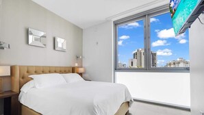 Habitación de hotel moderna con una cama grande, un televisor montado en la pared y vistas a la ciudad a través de la ventana.