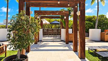 Une pergola en bois décorée de guirlandes lumineuses, un arbre en pot et des sièges d’extérieur.