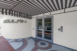A building entrance with a glass door, a metal sign above the door, and a patterned floor.