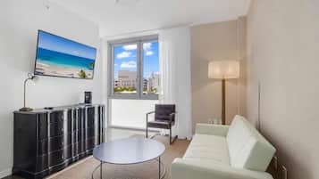 Une chambre d’hôtel moderne dotée d’une grande fenêtre, d’un téléviseur à écran plat, d’un meuble de rangement noir, d’un canapé blanc et d’une table basse ronde.