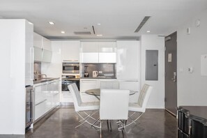 A modern kitchen with white cabinetry, stainless steel appliances, and a glass dining table with white chairs.
