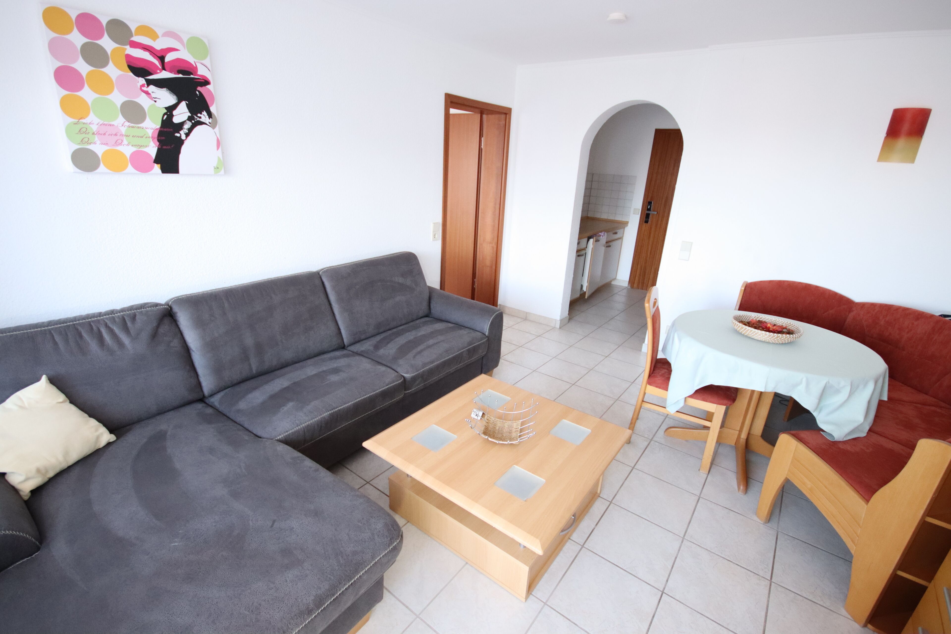 A living room with a grey sofa, a wooden coffee table, a red sofa, and a small dining table with chairs.