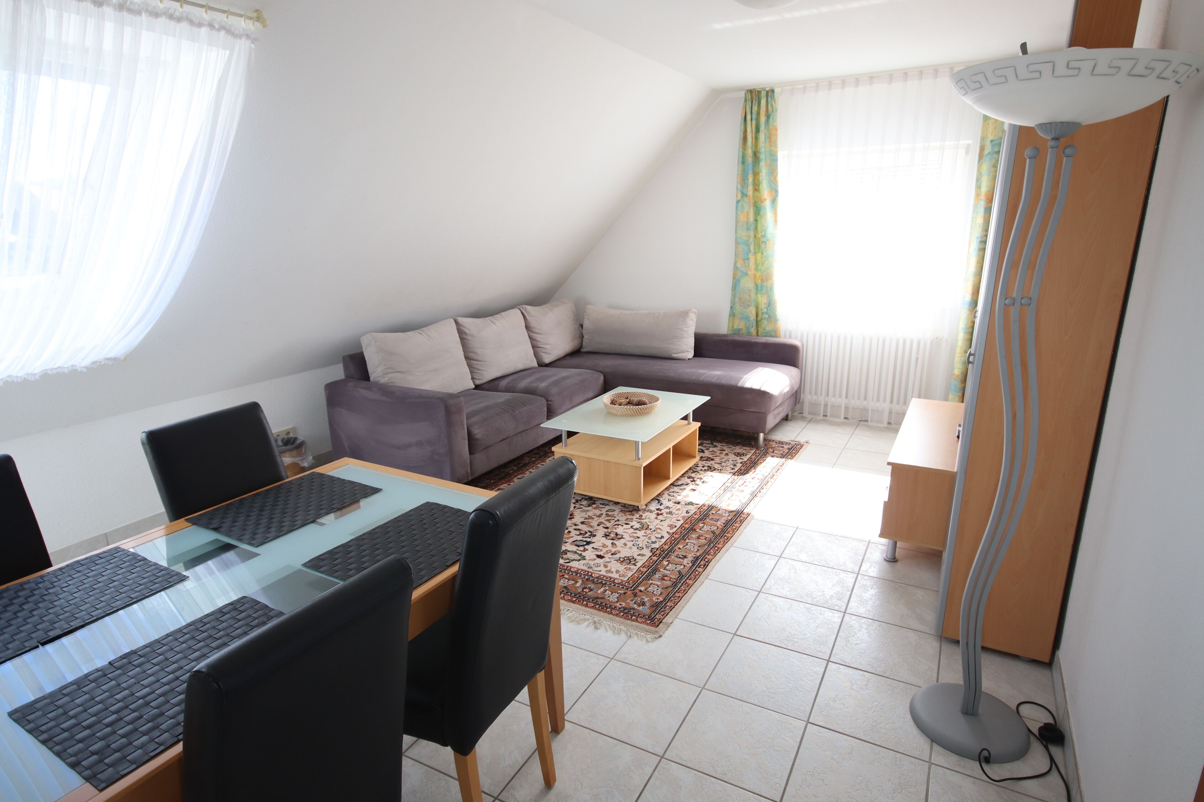 Una sala de estar moderna con una mesa de comedor de vidrio, un sofá, una mesa de centro y una lámpara de pie.