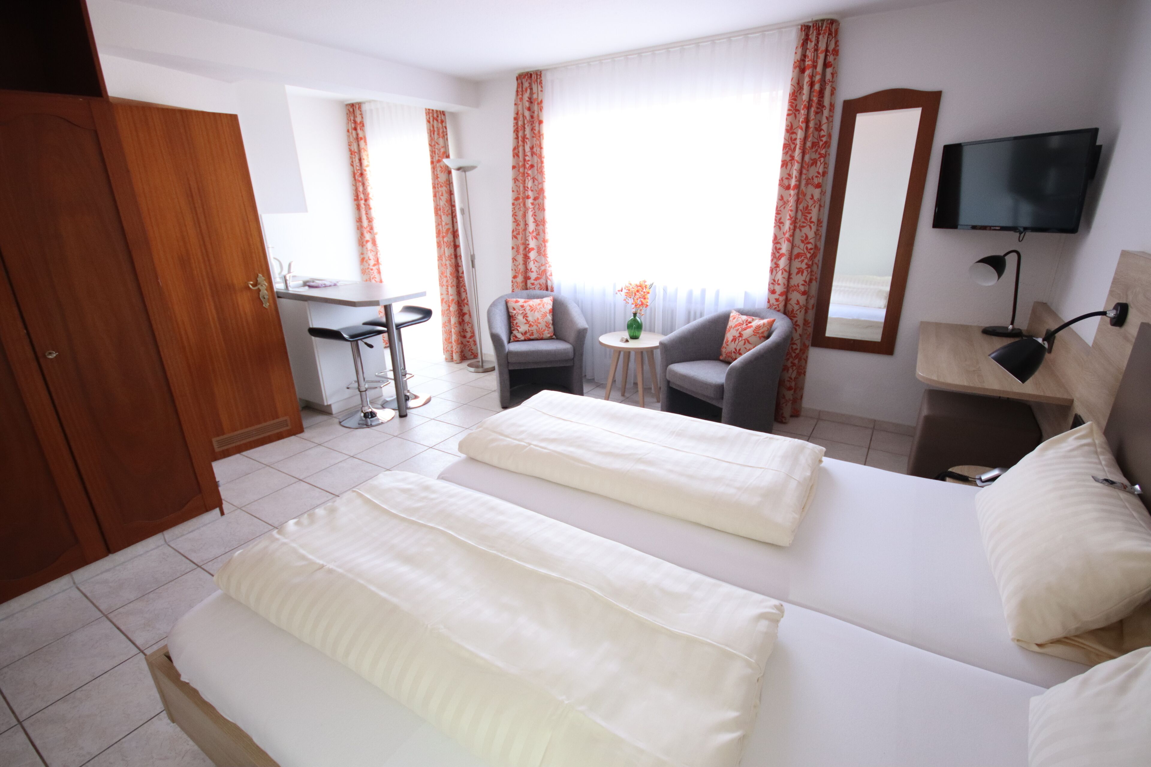 A hotel room with two beds, a desk, a chair, a TV, and a window with curtains.