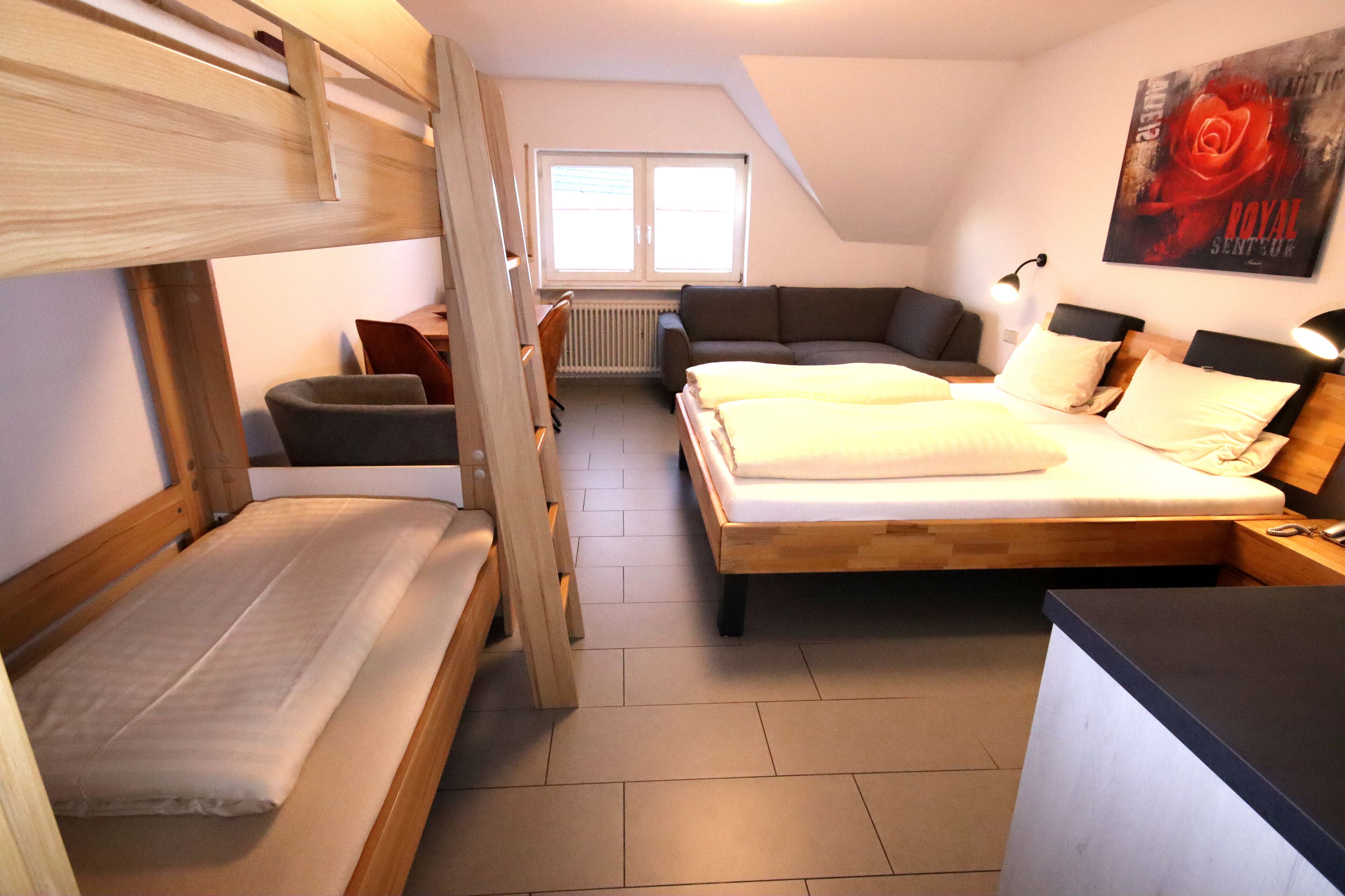 Een slaapzaal met stapelbedden, een bank, een bureau en een groot raam.