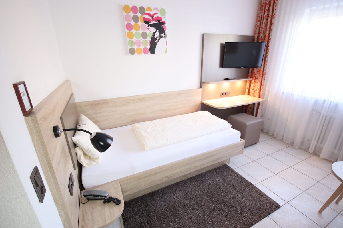Una habitación de hotel moderna con una cama de madera, un escritorio con silla, un televisor de pantalla plana y una obra de arte colorida en la pared.