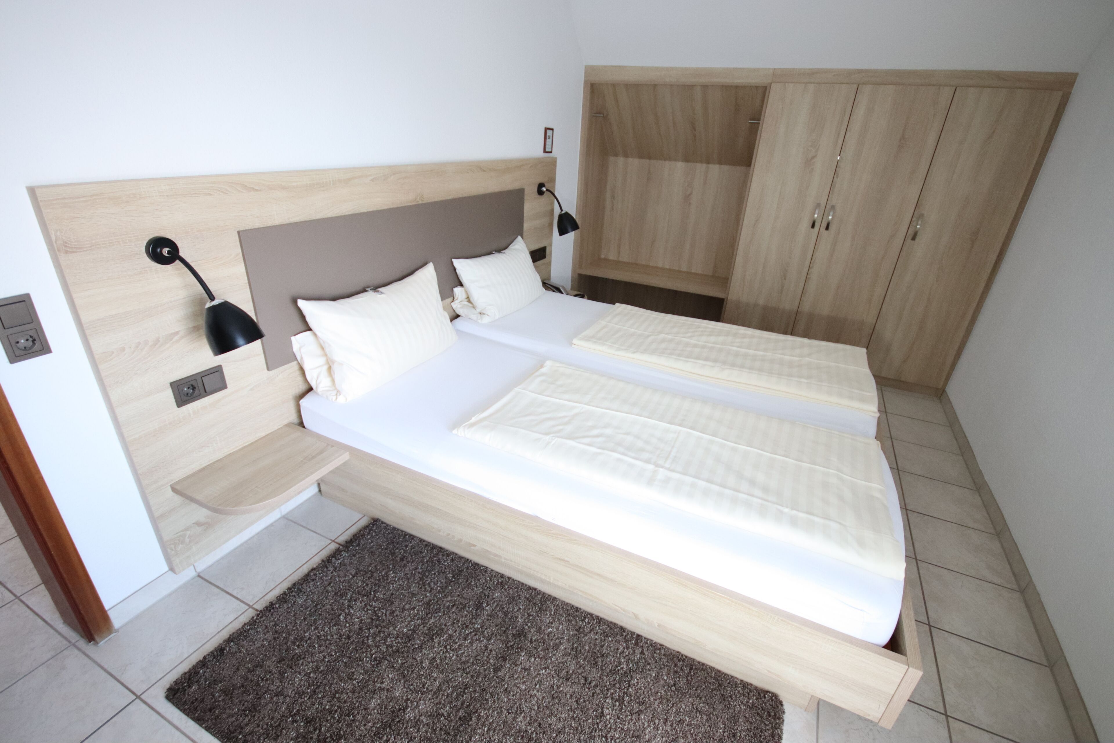 A bedroom with two beds, a wooden headboard, a bedside table, a lamp, and a wardrobe.