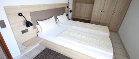 A bedroom with two beds, a wooden headboard, a bedside table, a lamp, and a wardrobe.