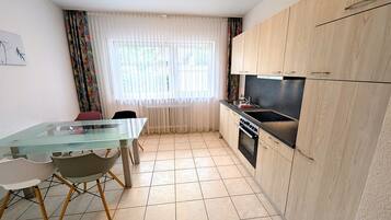 A compact kitchen with a glass dining table, wooden cabinets, and a built-in oven.