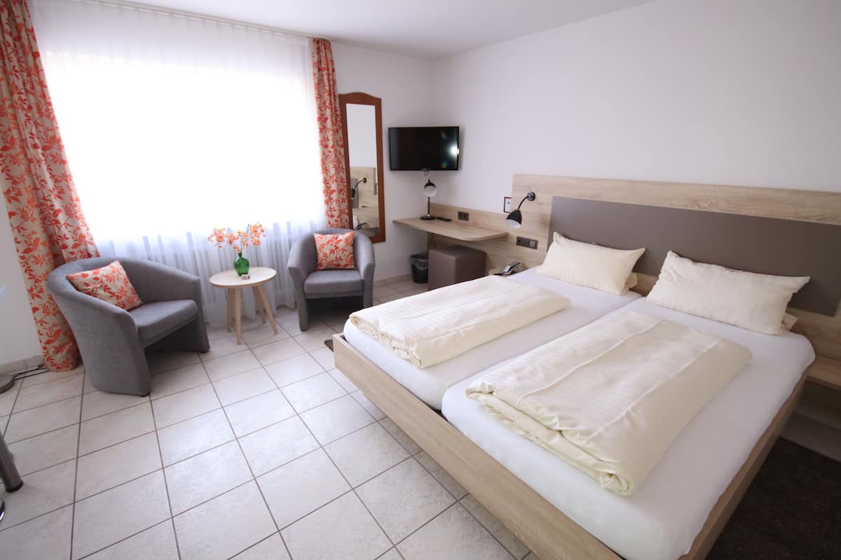 Una habitación de hotel con una cama grande, un escritorio, una silla, un televisor y una ventana con cortinas.