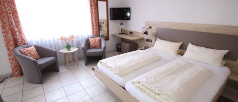 A hotel room with a large bed, a desk, a chair, a TV, and a window with curtains.